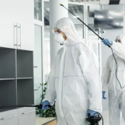 2 personnes en combinaison de protection vaporisant un produit sur des murs