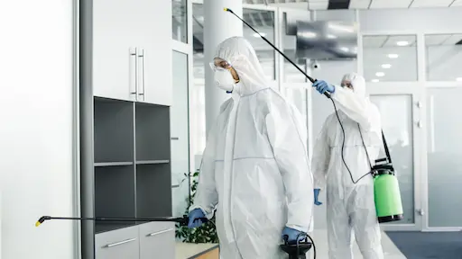 2 personnes en combinaison de protection vaporisant un produit sur des murs